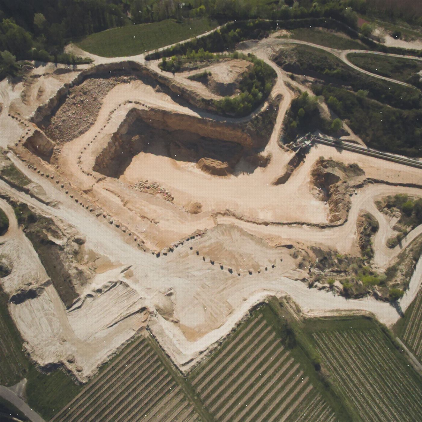 Aerial view of large-scale earthworks and quarry platforms beside vineyard fields